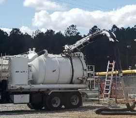 A white vacuum truck with a raised arm, used for industrial cleanup outdoors.