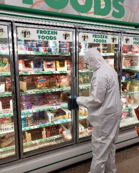 Person in hazmat suit pouring granules on floor near a red barrel.