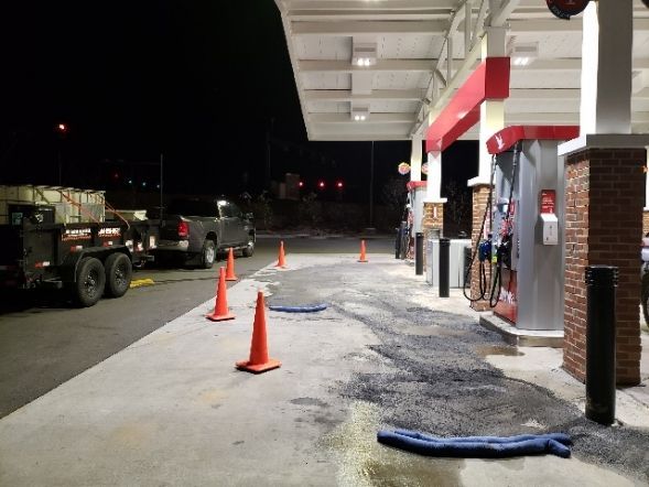 Gas station at night with spill, marked by cones. 