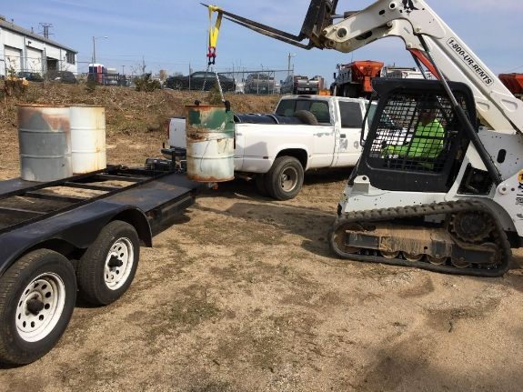 Workers in protective gear clean up an oil spill, scooping oil into black bags, in a murky, black environment.