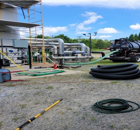 Empty warehouse interior with three figures standing in the doorway, sunlight streaming in.