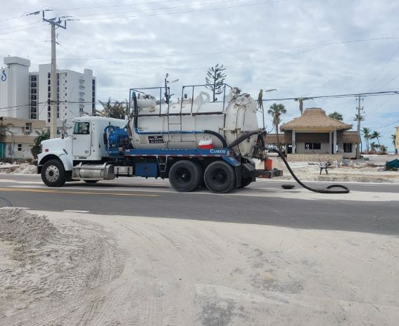 White vacuum truck on road, extracting waste. 