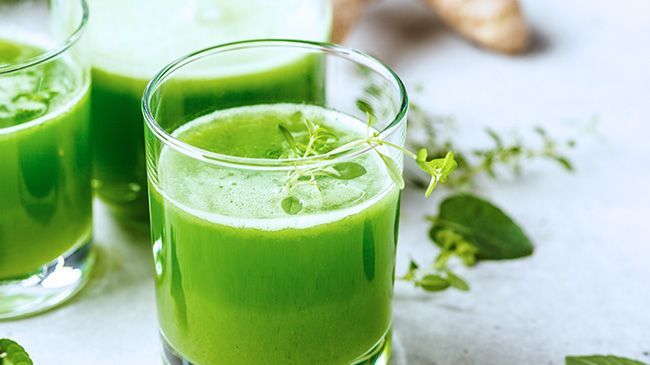 A close up of three glasses of green juice on a table.