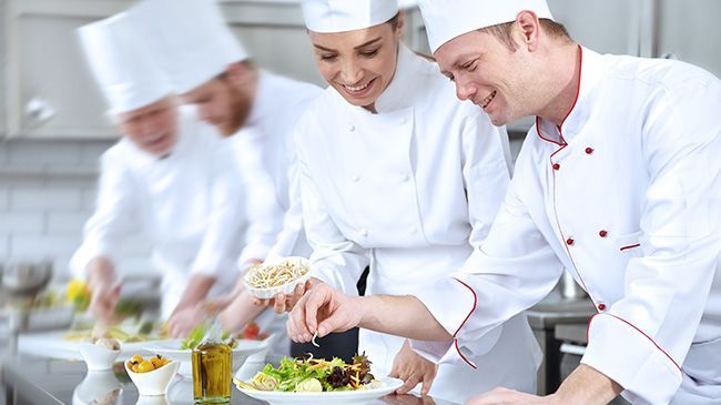 A group of chefs are standing in a kitchen talking to each other.