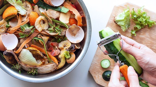 A person is peeling vegetables in a bowl next to a cutting board.