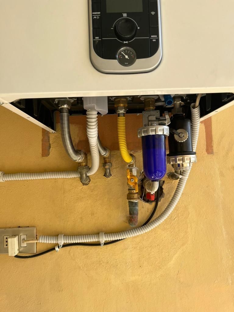 Caldaia a gas con tubi collegati e filtri contro una parete gialla.