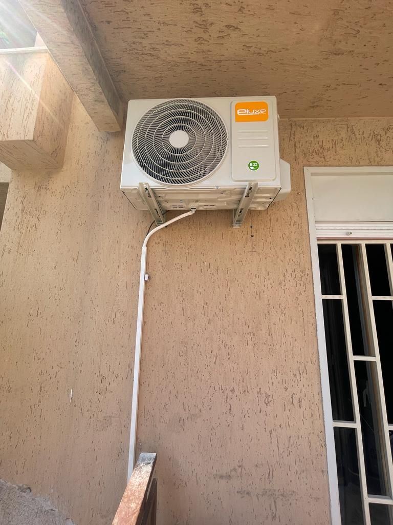 Condizionatore d'aria montato su una parete in stucco beige accanto a una finestra con sbarre bianche.