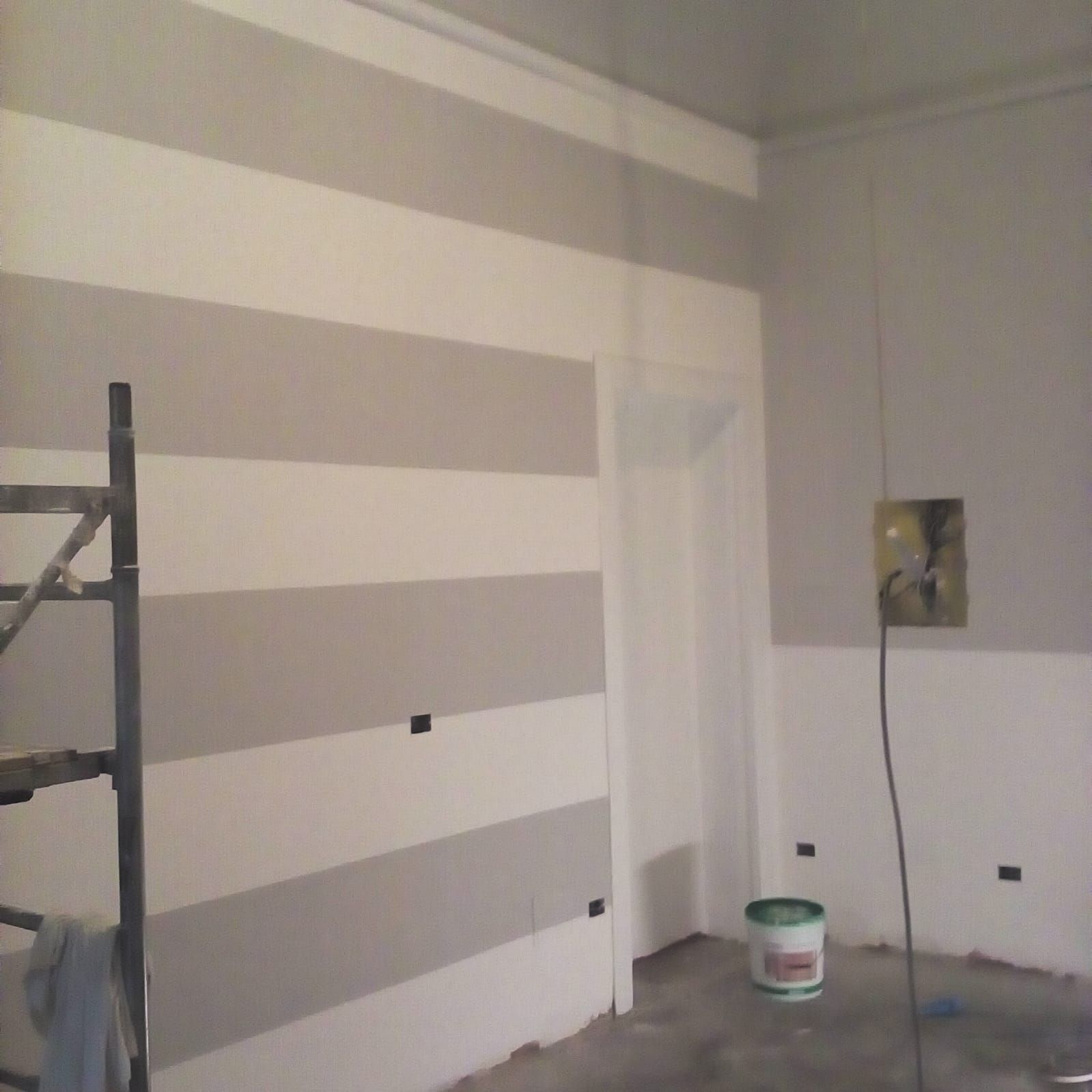 Interno della stanza con pareti a strisce grigie e bianche, porta e una scala di metallo.