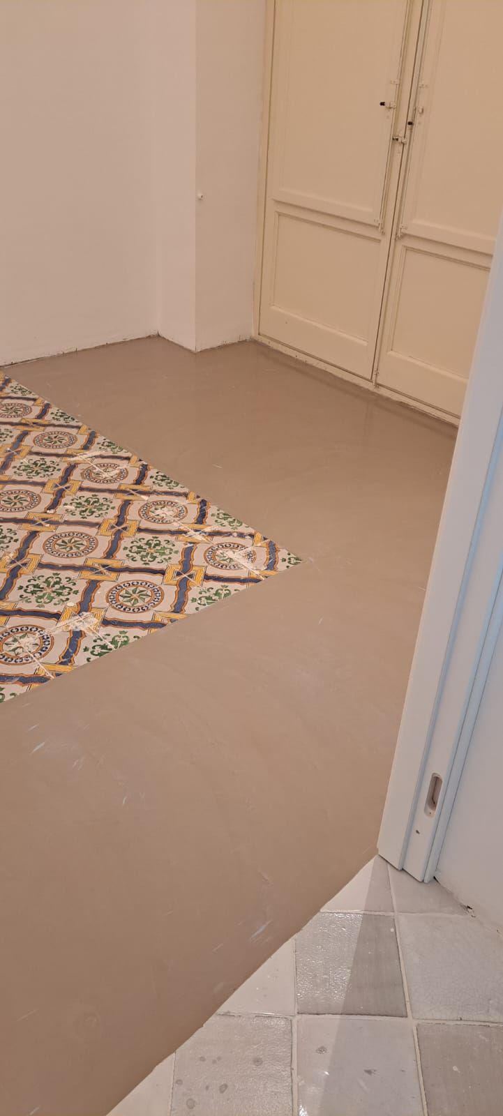 Una stanza con pavimento in piastrelle a fantasia e pavimento beige neutro. Una porta beige chiaro sullo sfondo.