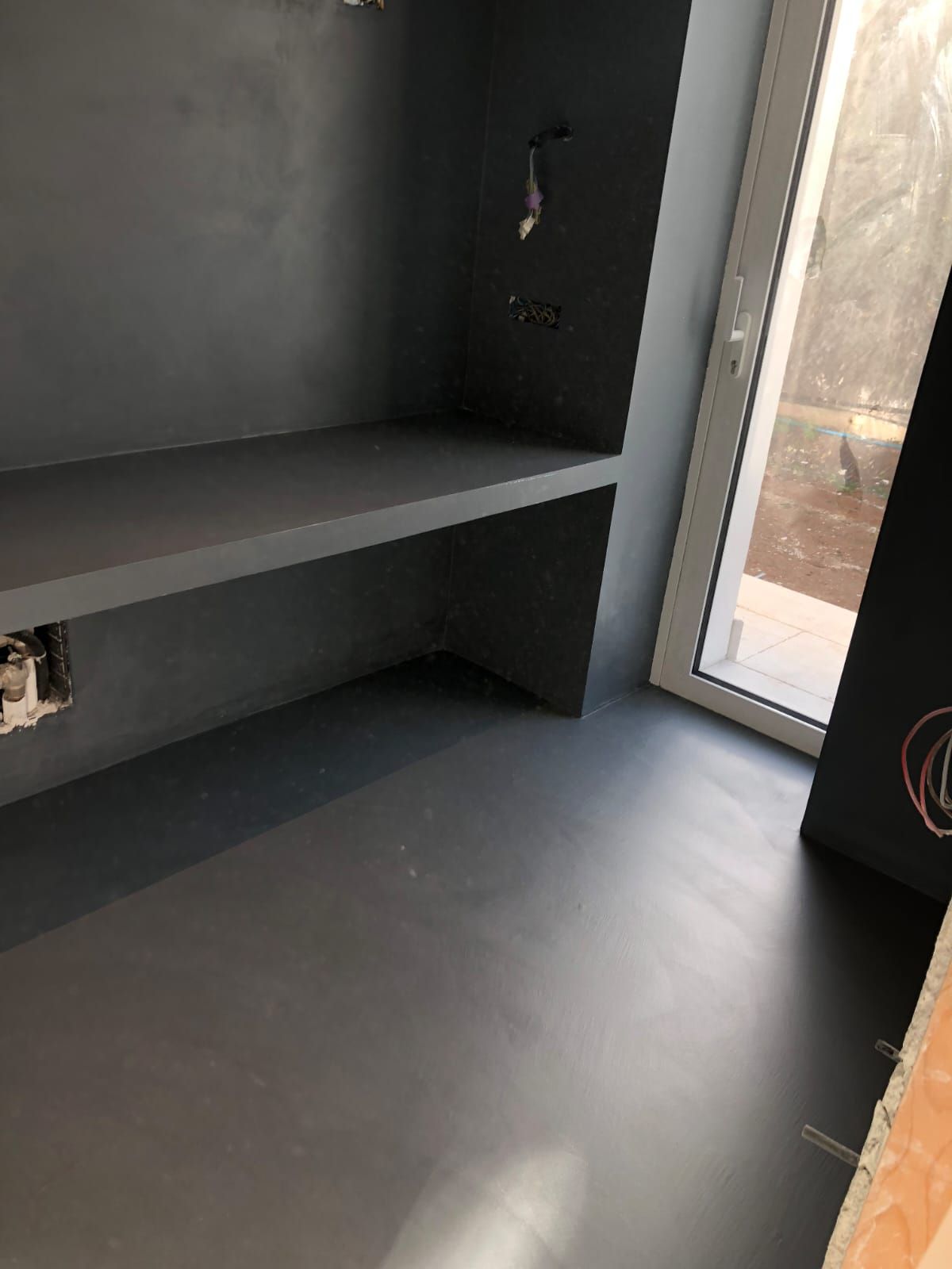 Una piccola stanza con pareti grigie, un bancone incorporato e una finestra; anche il pavimento è grigio.