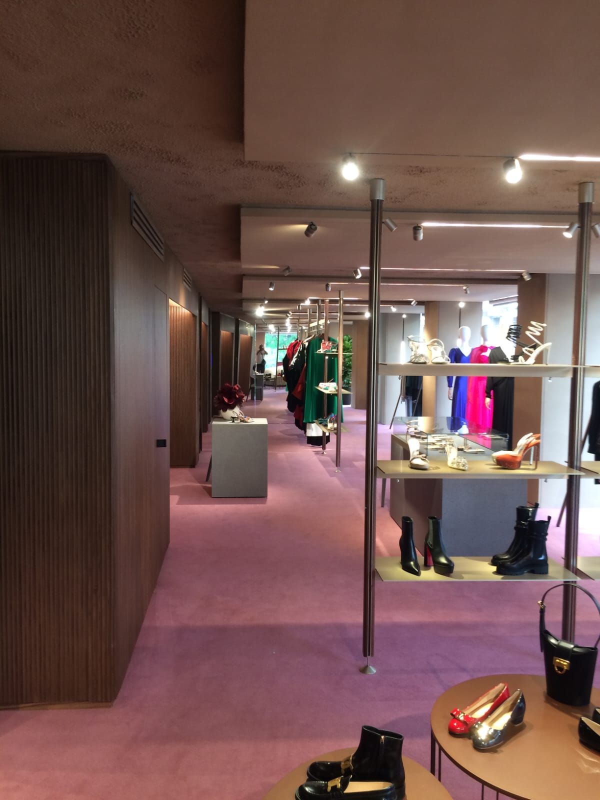 L'interno di un negozio di lusso. Moquette rosa, appendiabiti, scaffali con scarpe e pareti dai toni neutri.