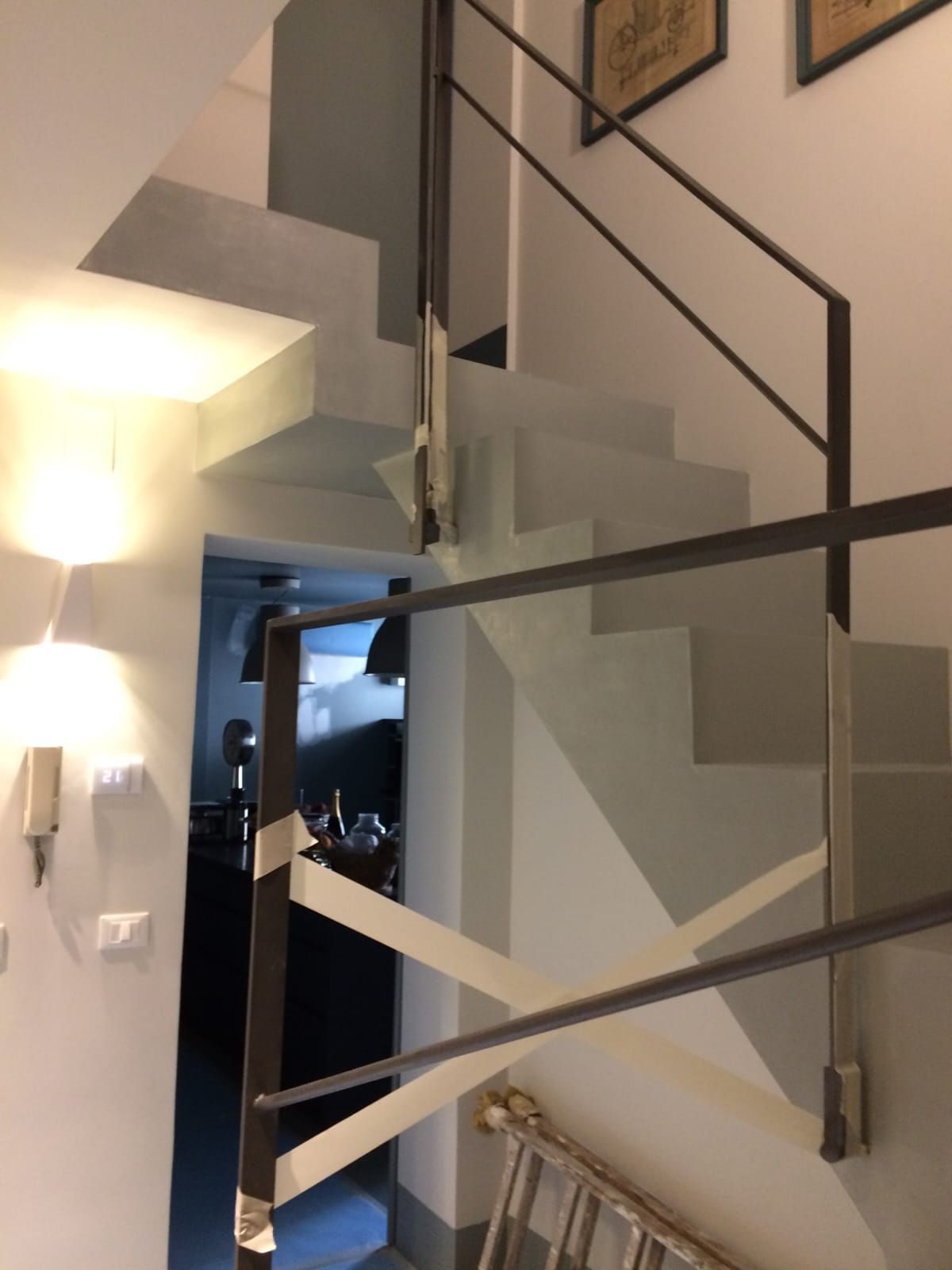 Scala con gradini grigi e ringhiera in metallo nero, interni dai toni neutri.