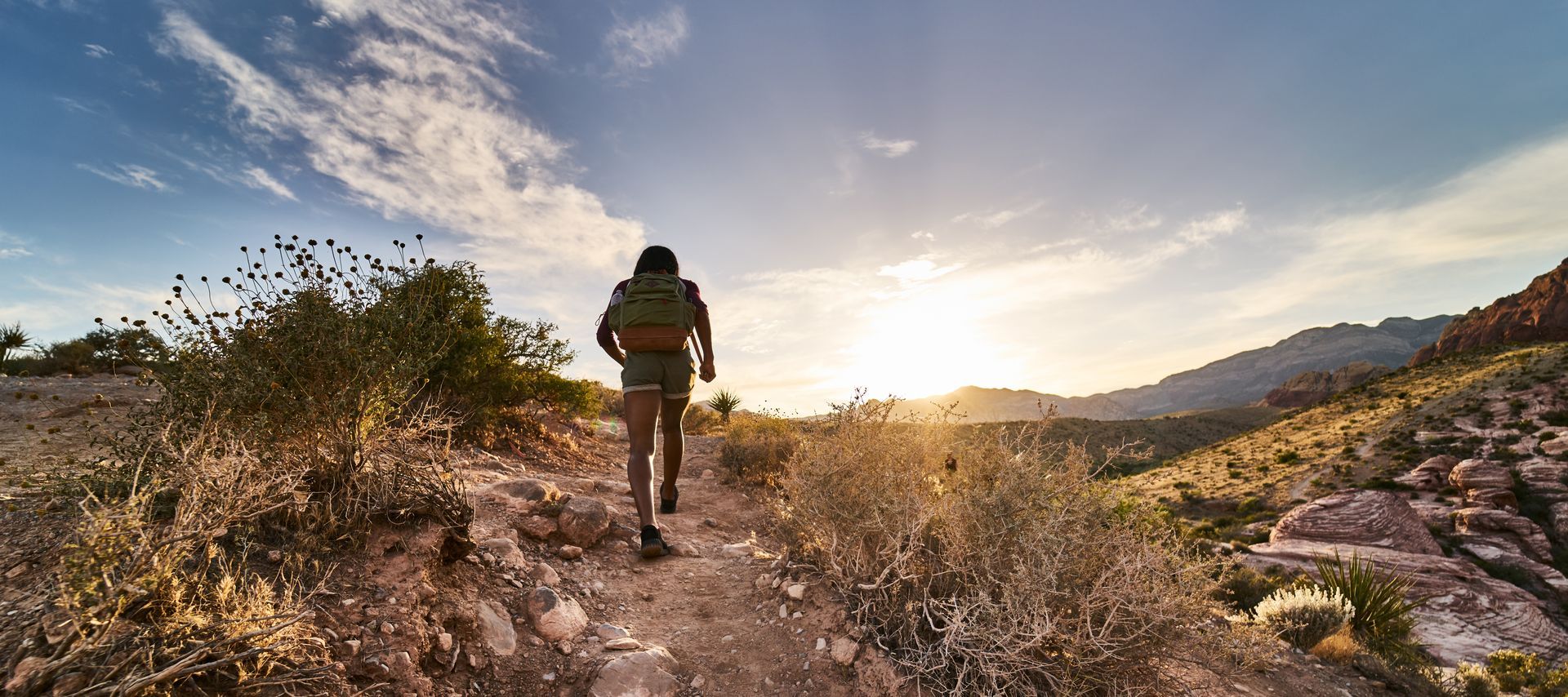 A person is walking down a dirt path in the mountains at sunset.