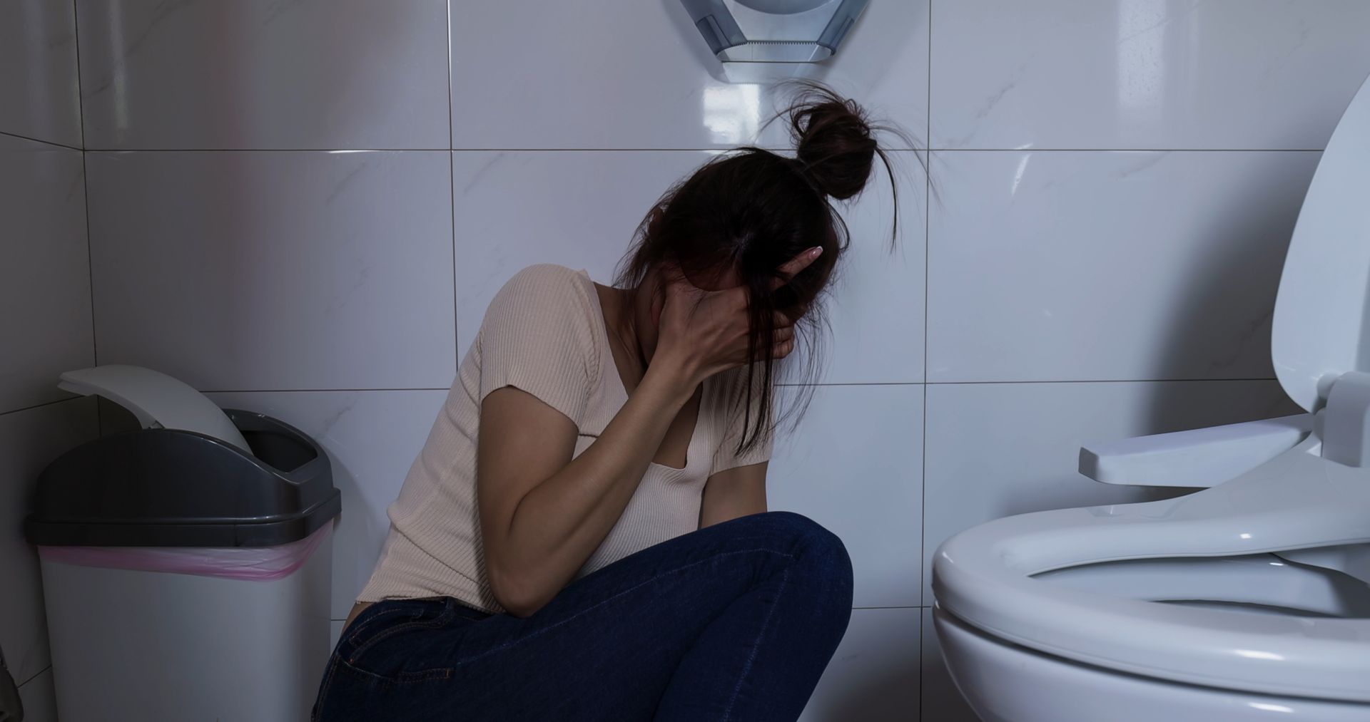 A woman is kneeling in a bathroom next to a toilet.