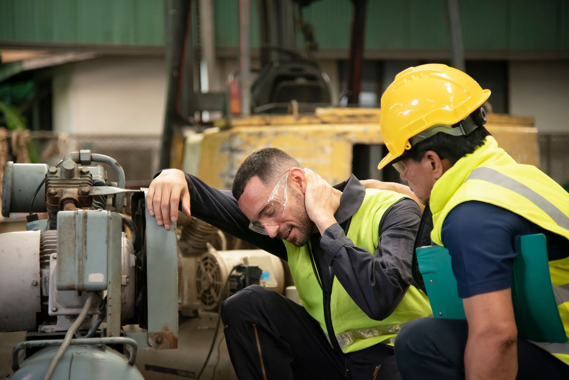 Two construction workers are working on a machine in a factory.