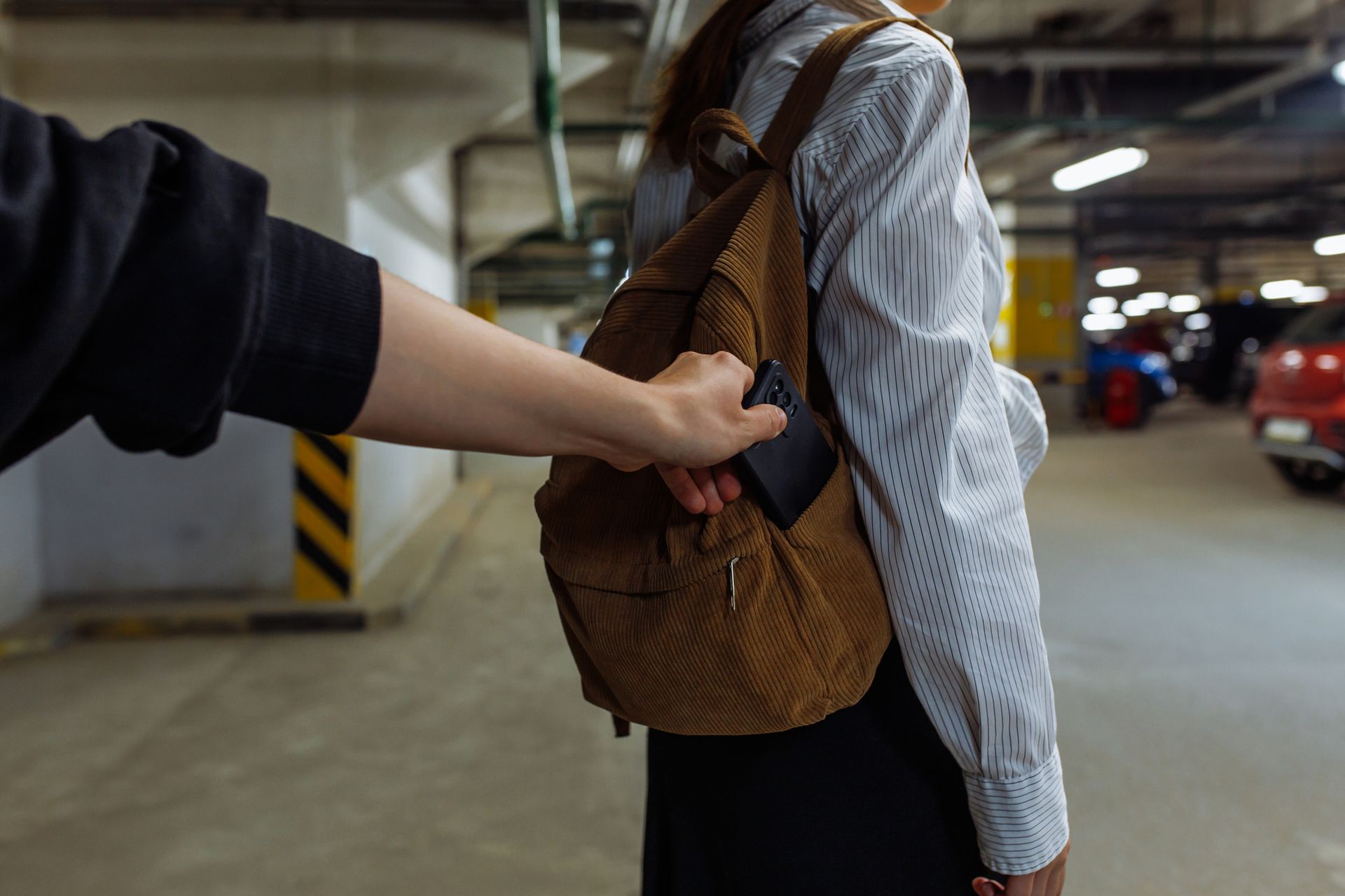 A man is stealing a wallet from a woman 's backpack in a parking garage.