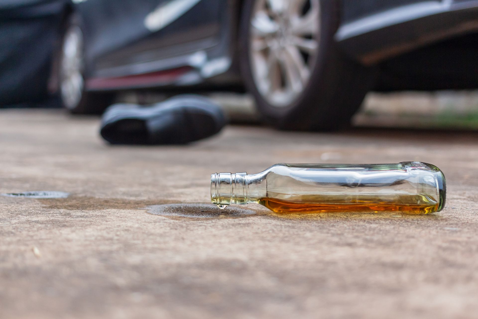 A bottle of alcohol is laying on the ground in front of a car.