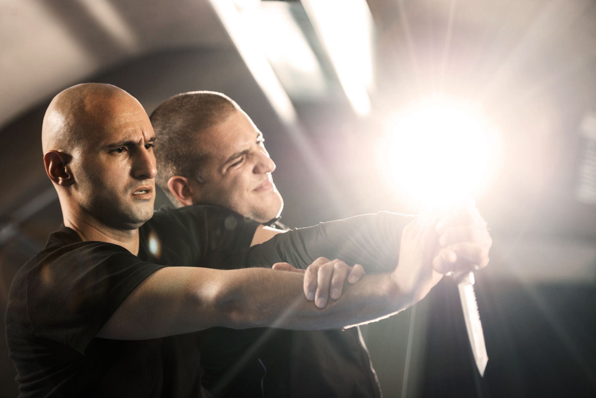 Two men are practicing martial arts together in a dark room.