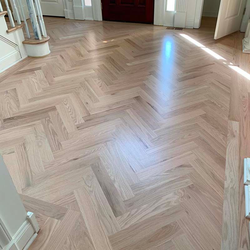 A herringbone wood floor in a living room with stairs.