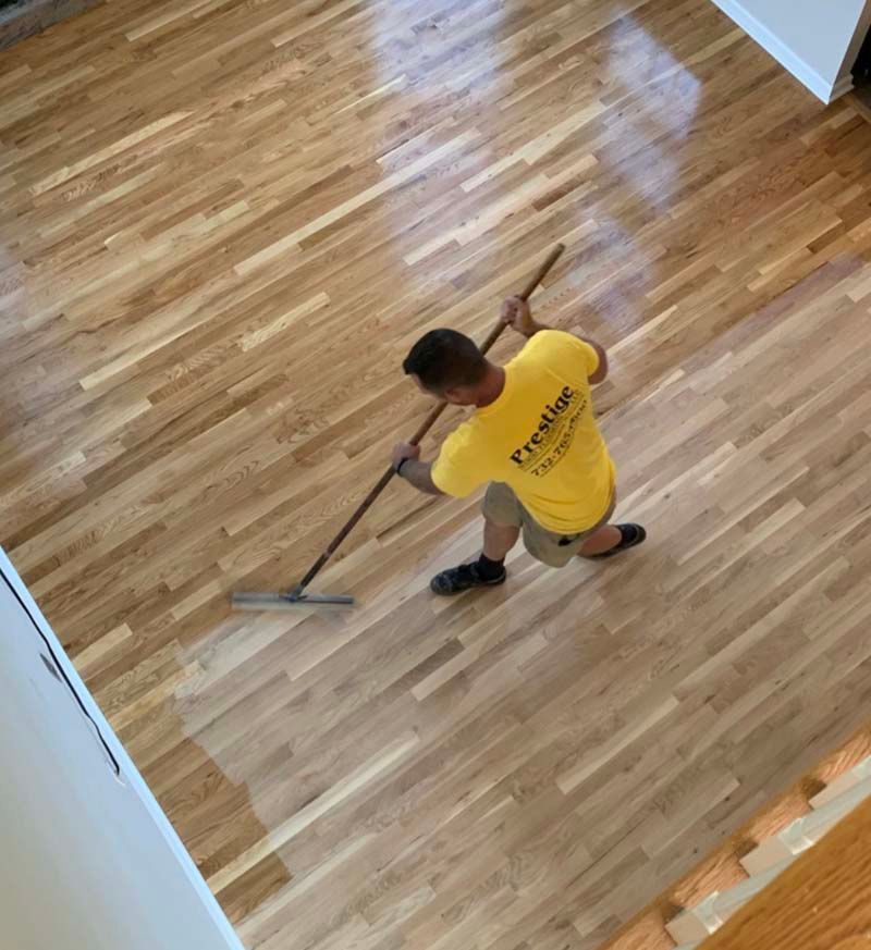 A man wearing a yellow shirt that says prestige is sweeping a wooden floor