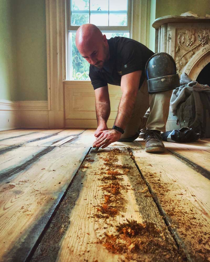 A man is working on a wooden floor in a room.