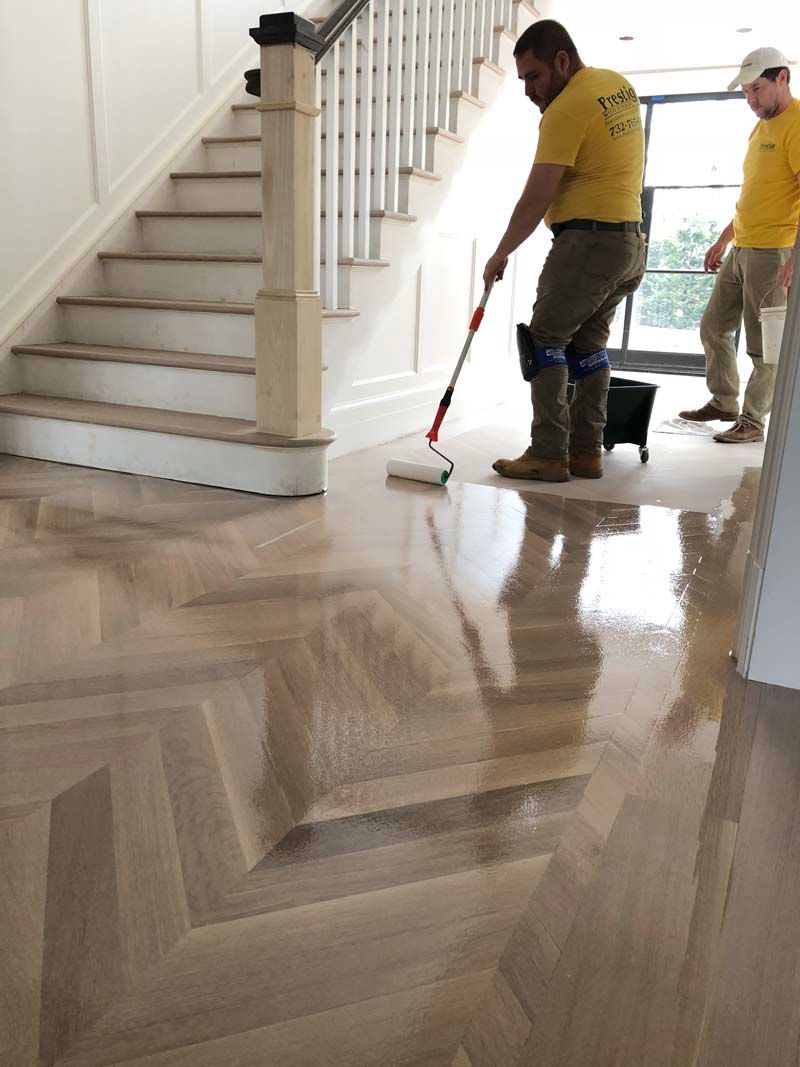 A man is painting a wooden floor with a roller.
