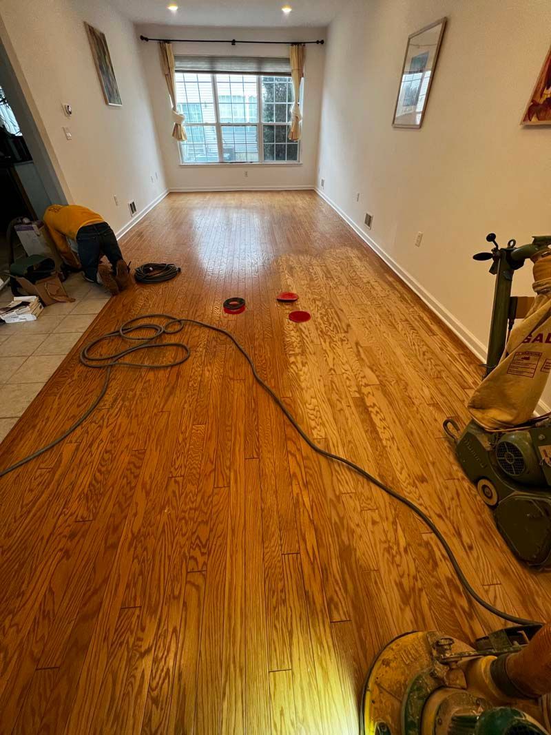 A person is sanding a wooden floor in a living room.