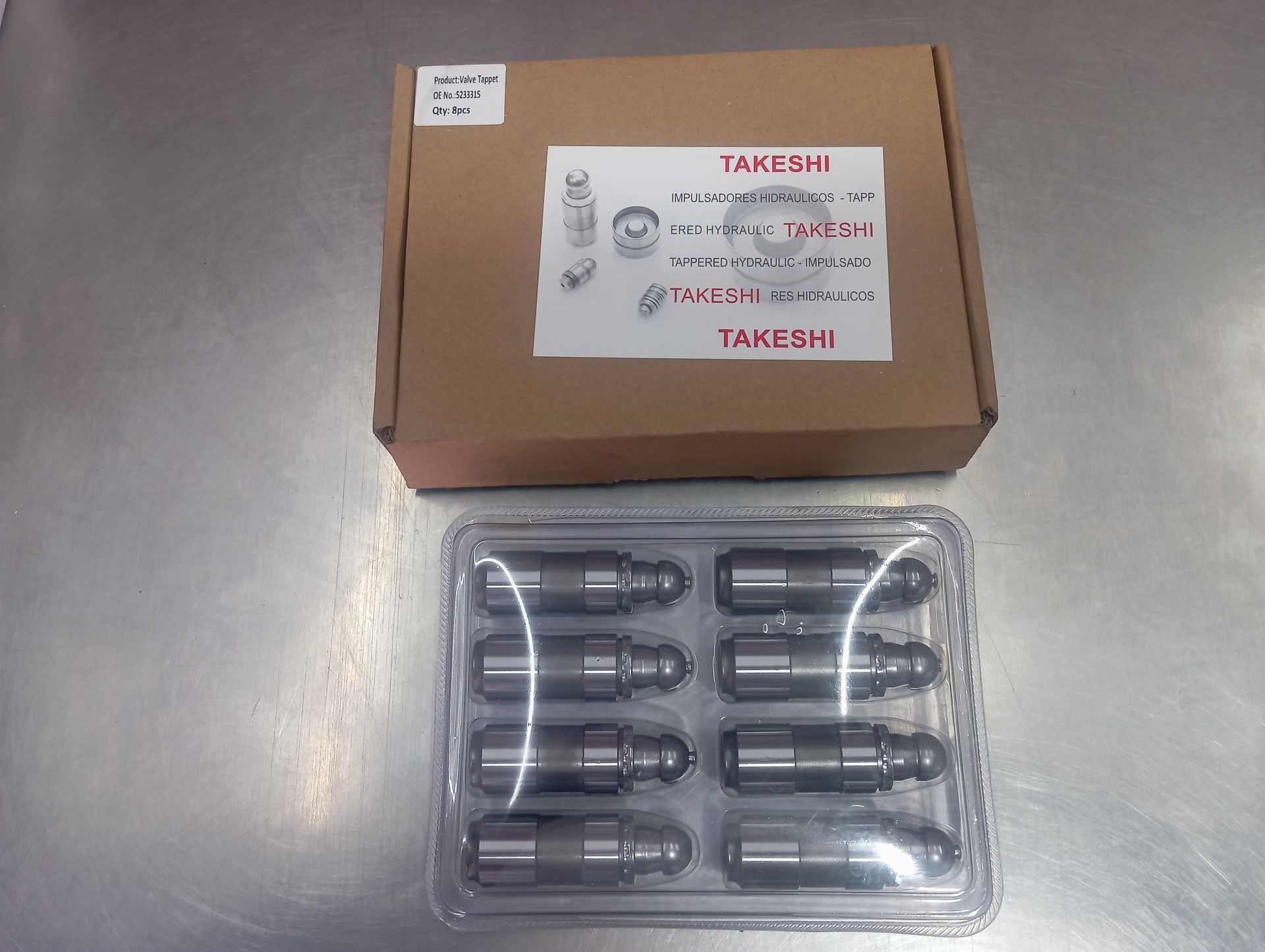 Caja marrón con una etiqueta sobre una bandeja de plástico transparente que contiene ocho piezas cilíndricas negras.