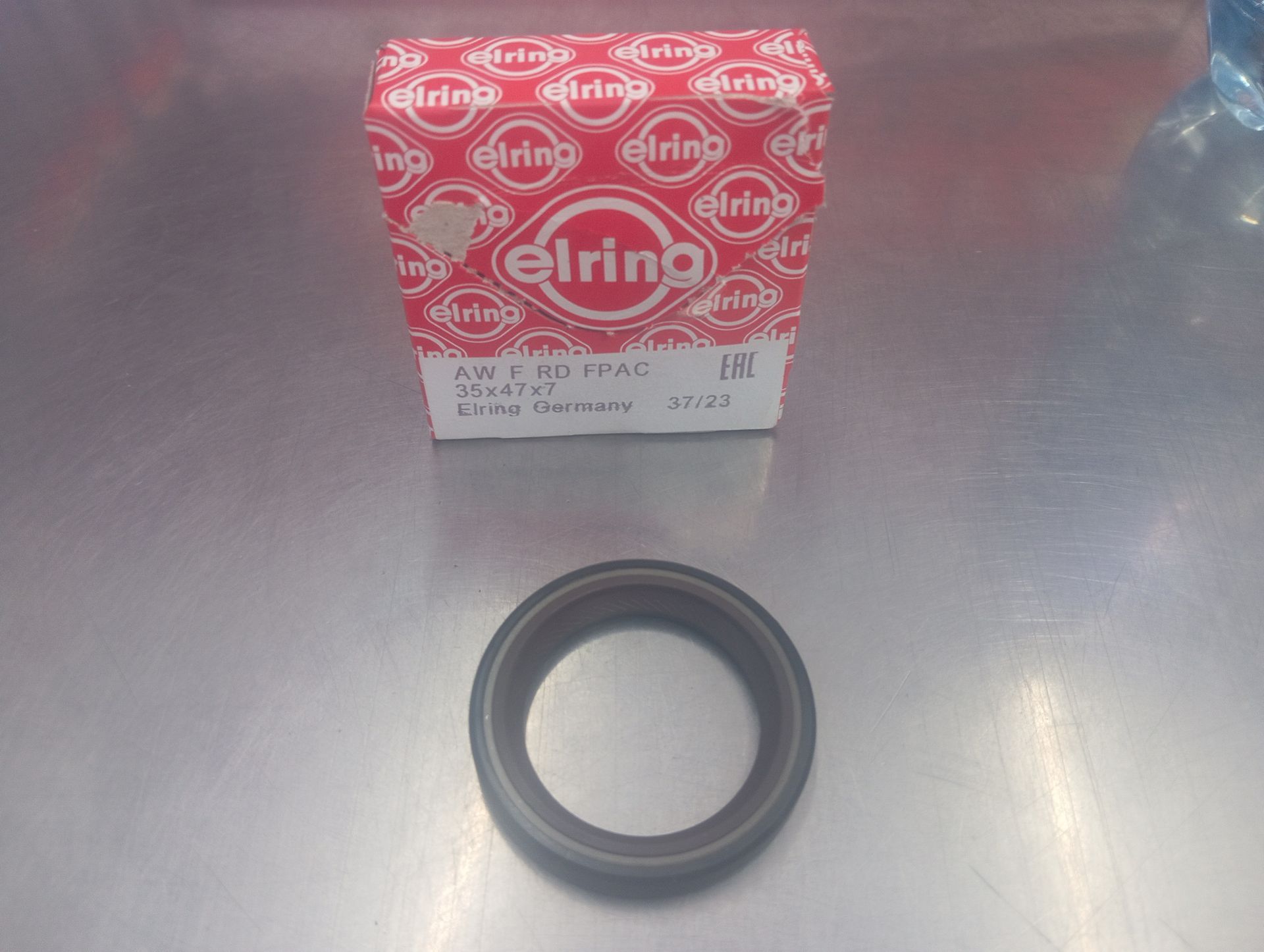 Caja roja de Elring sobre un sello circular negro en una superficie de acero inoxidable.