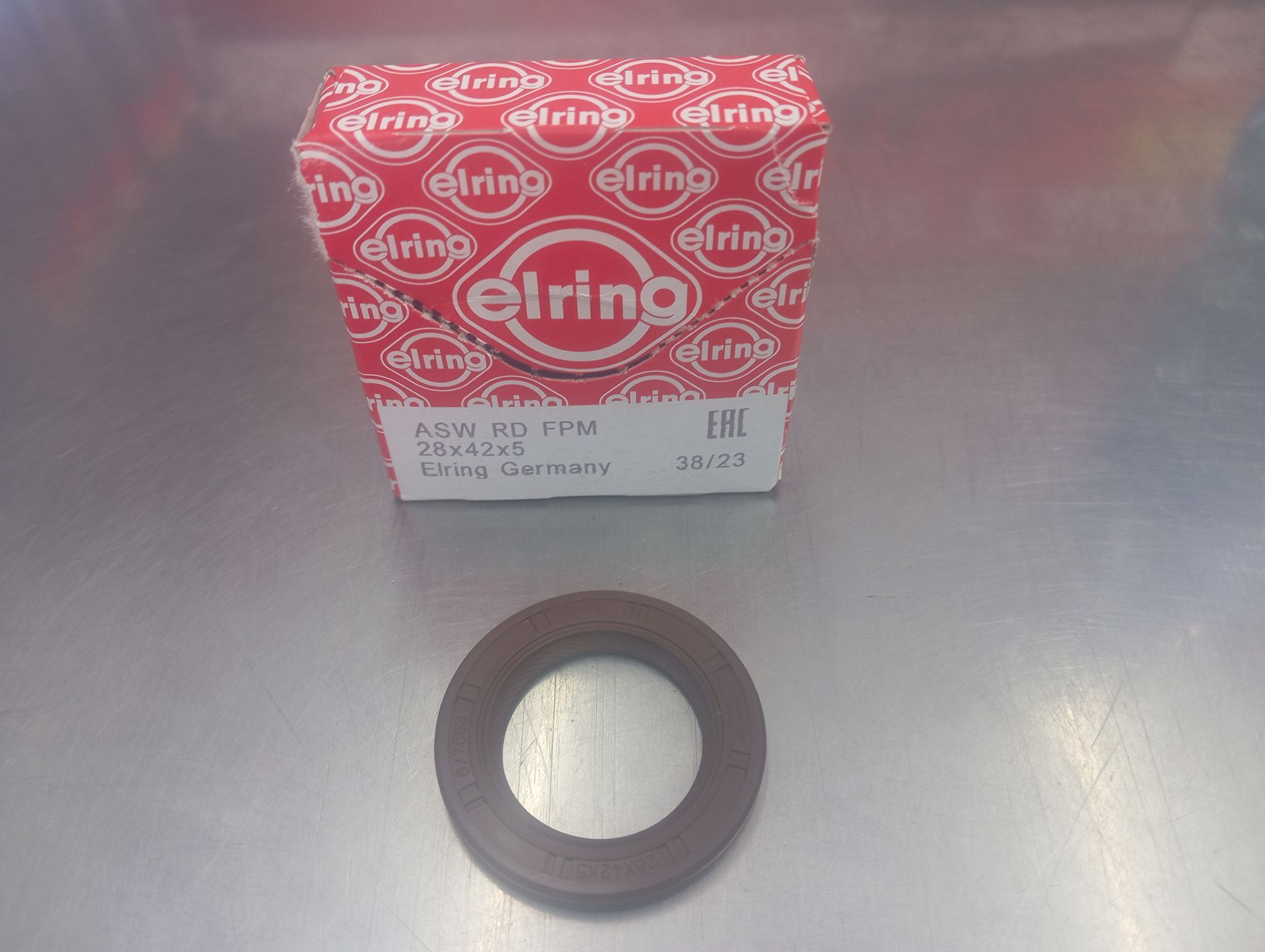 Caja roja de Elring sobre un sello circular negro en una superficie de acero inoxidable.