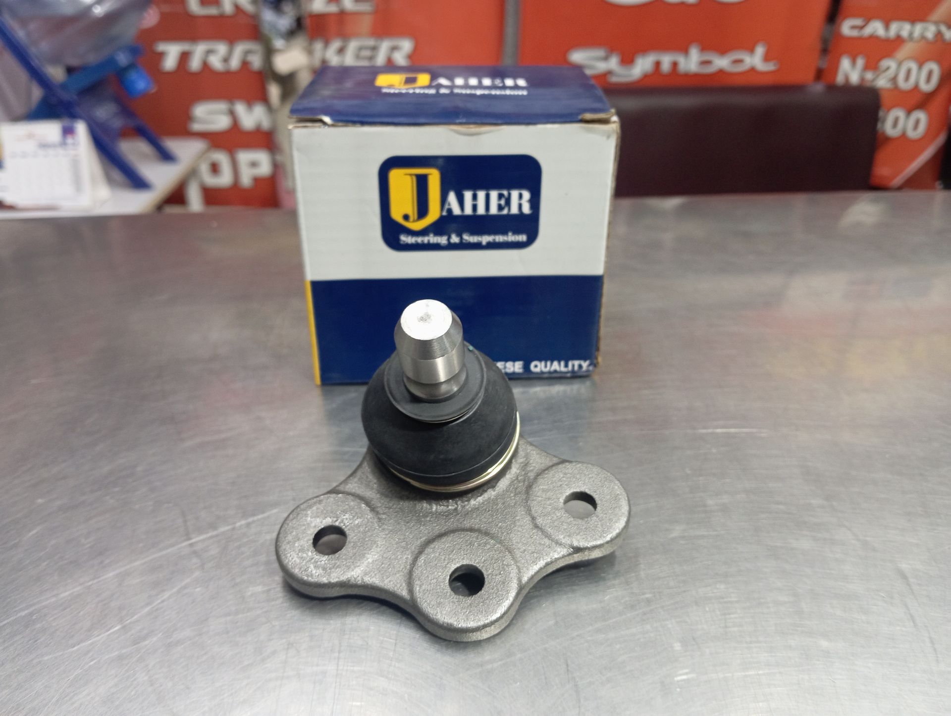 Rótula de automóvil sobre una superficie metálica con una caja Jaher al fondo.