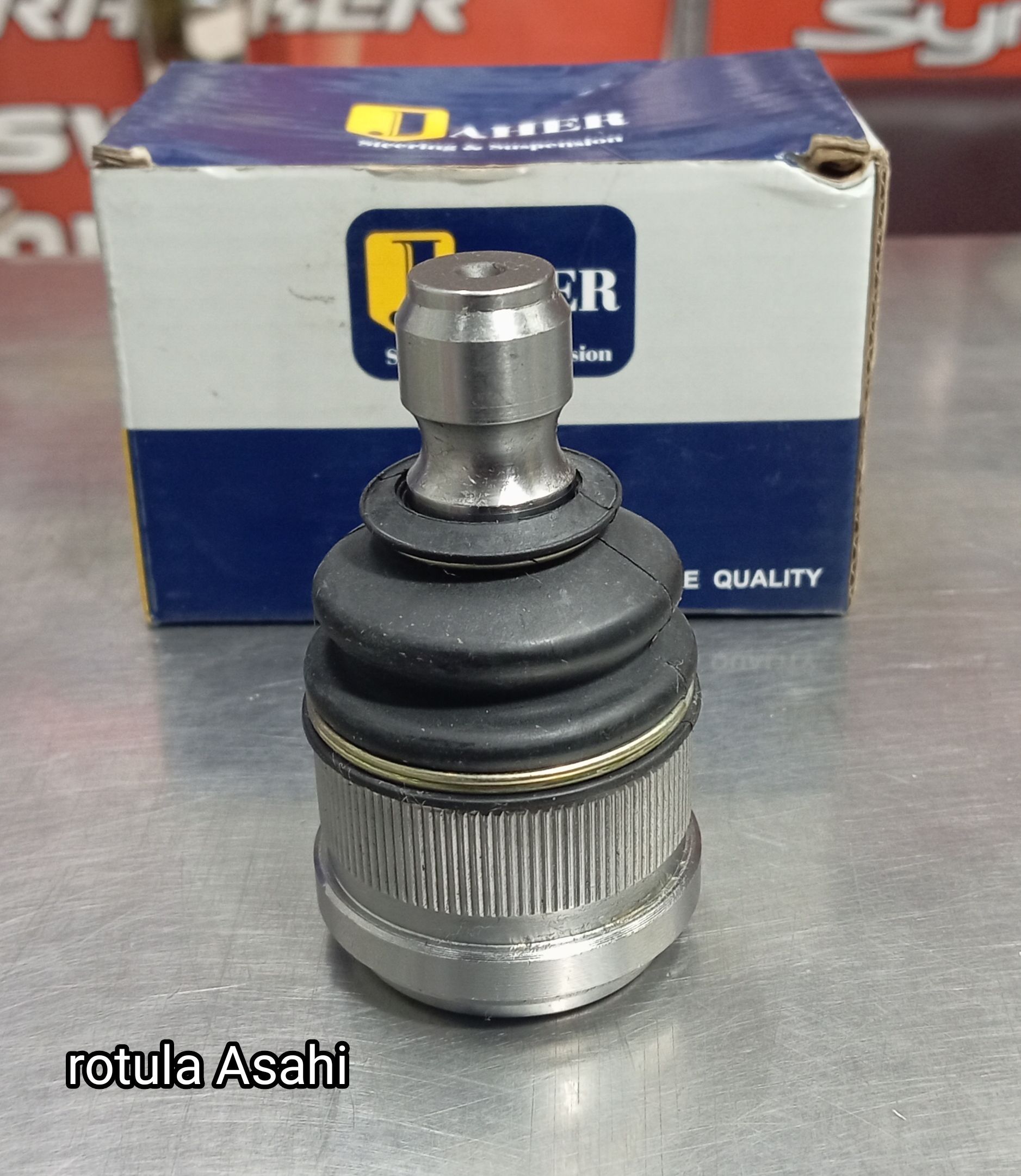 Rótula plateada para automóvil delante de una caja Asahi azul y blanca sobre una superficie blanca.