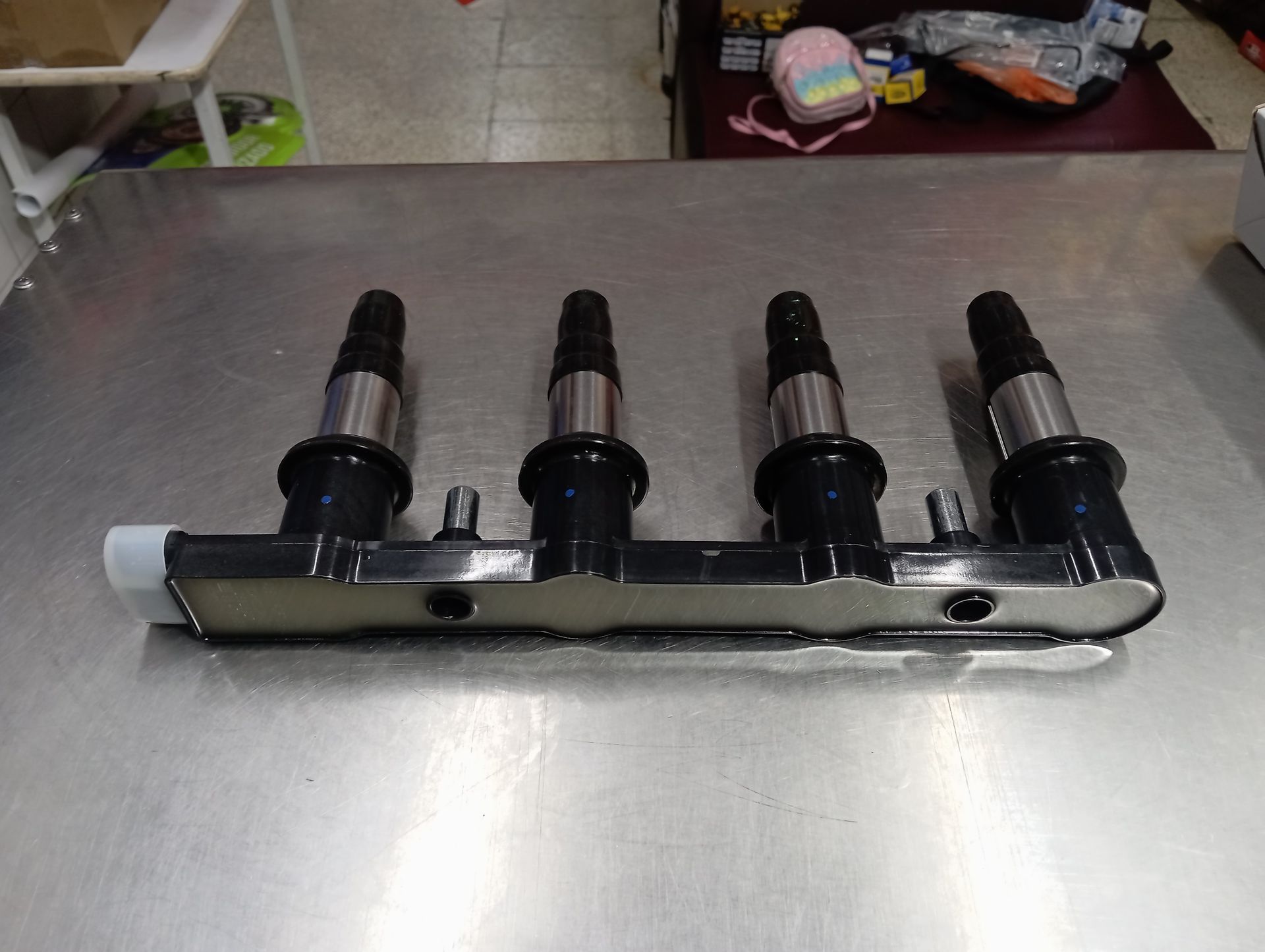 Riel de inyectores de combustible cromado con cuatro inyectores negros sobre una superficie metálica.