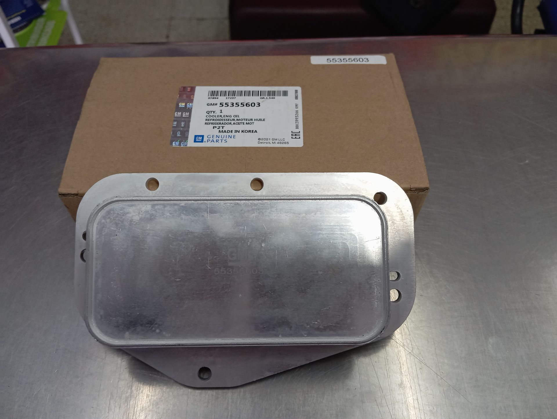 Pieza metálica con múltiples agujeros delante de una caja de cartón sobre una mesa.