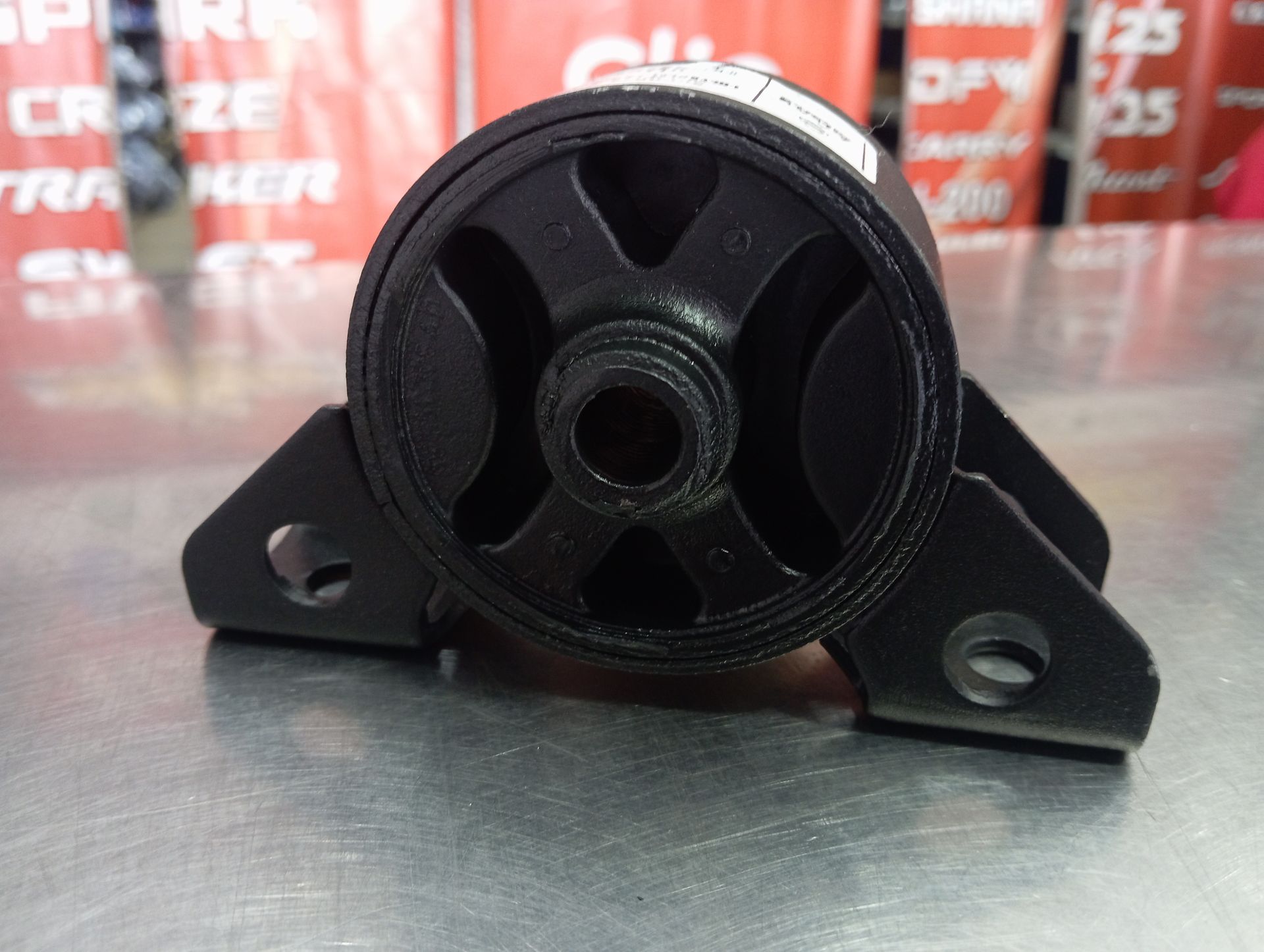 Soporte de motor de goma con dos orificios para tornillos sobre una superficie metálica, producto fotografiado en interiores.