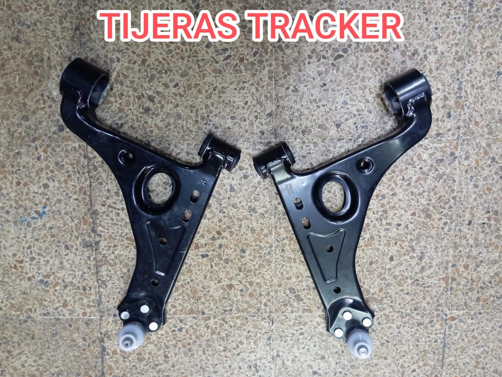 Brazos de control de suspensión negros para un Tracker, exhibidos sobre un piso de concreto.