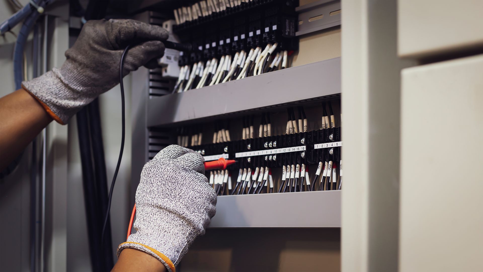 A person wearing gloves is working on an electrical box.