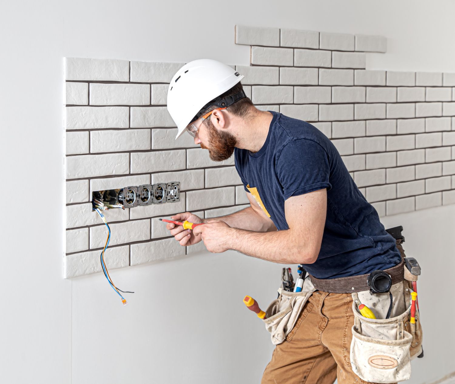 A man is working on an electrical outlet on a brick wall.
