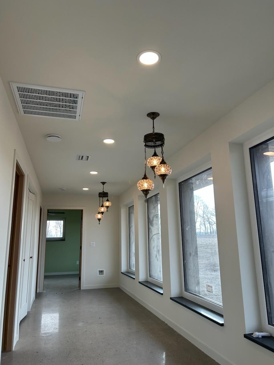 A long hallway with a lot of windows and lamps hanging from the ceiling.