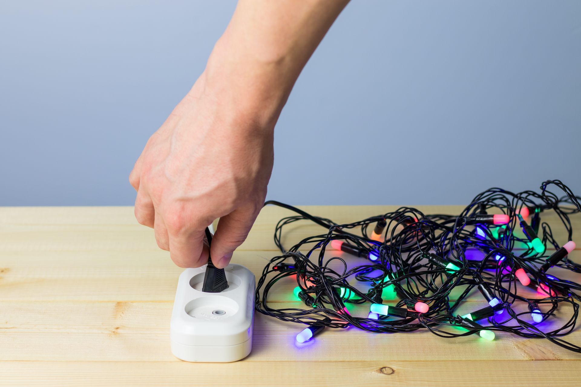 Hand plugging Christmas lights into a white outlet on a wooden surface.