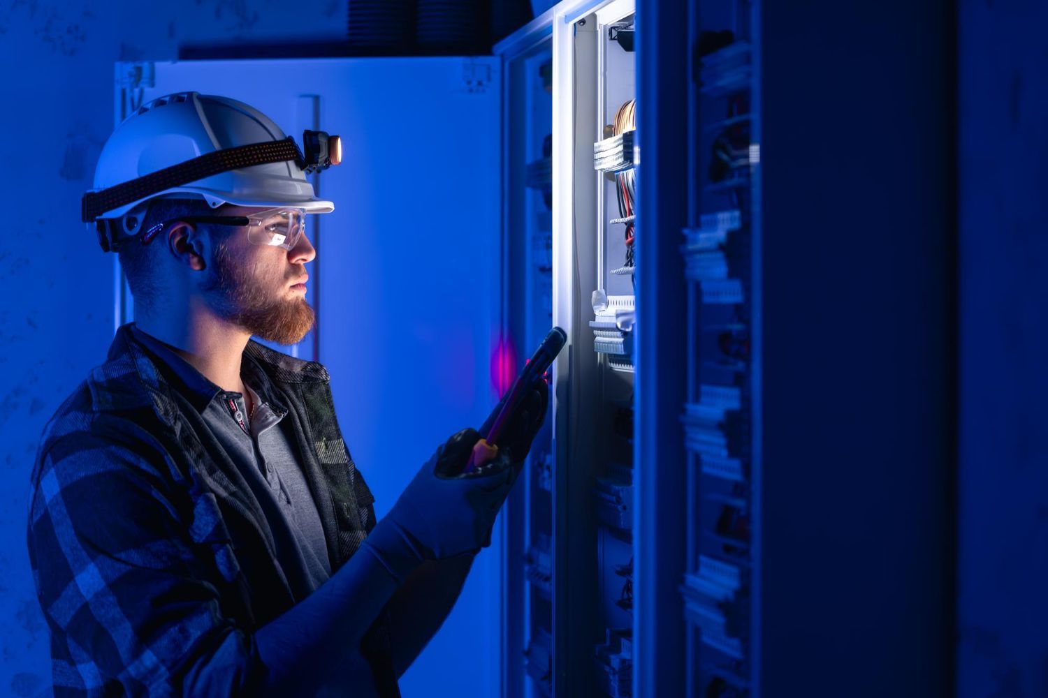 A man wearing a hard hat and safety glasses is working on a server.