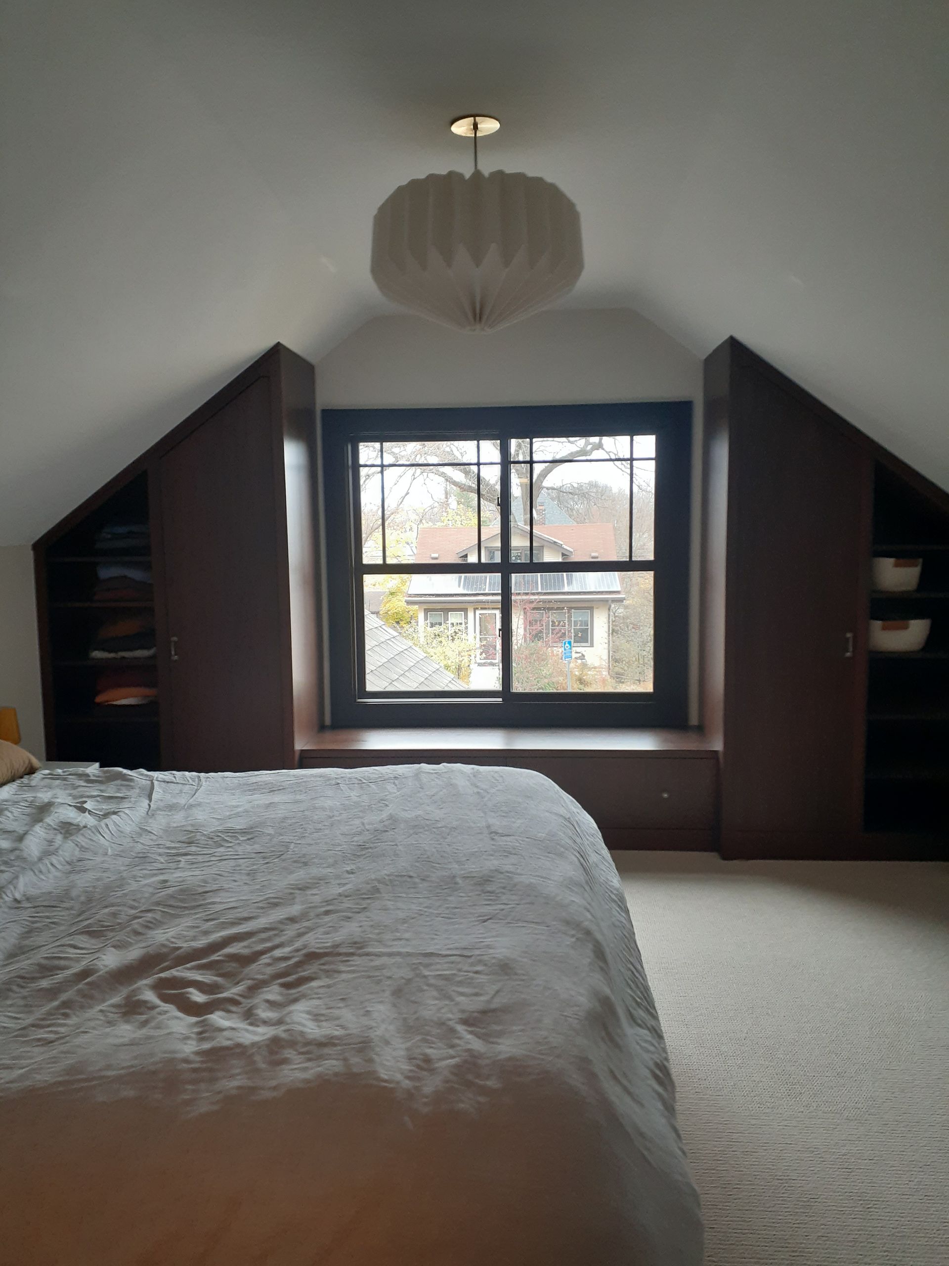 A bedroom with a bed and a window with a view of a house.