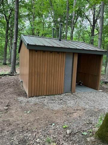 A small wooden shed with a metal roof in the middle of a forest.