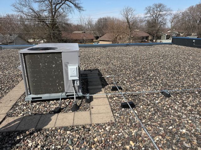 An air conditioner is sitting on top of a gravel roof.