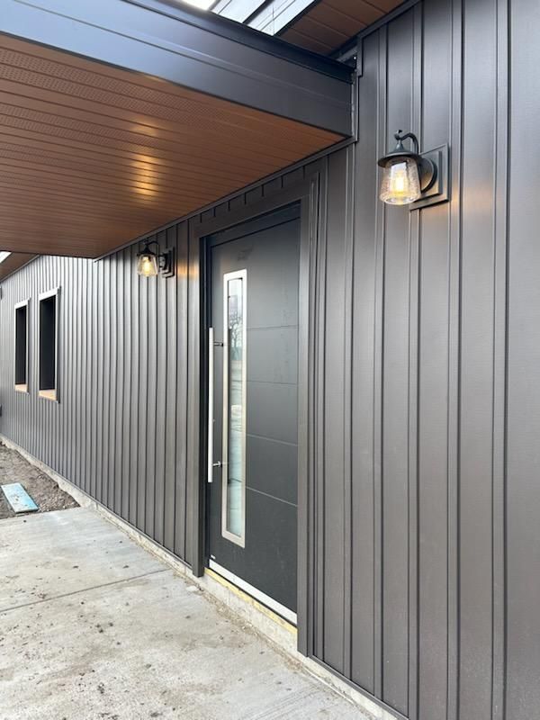 A gray house with a black door and a light on the side of it.