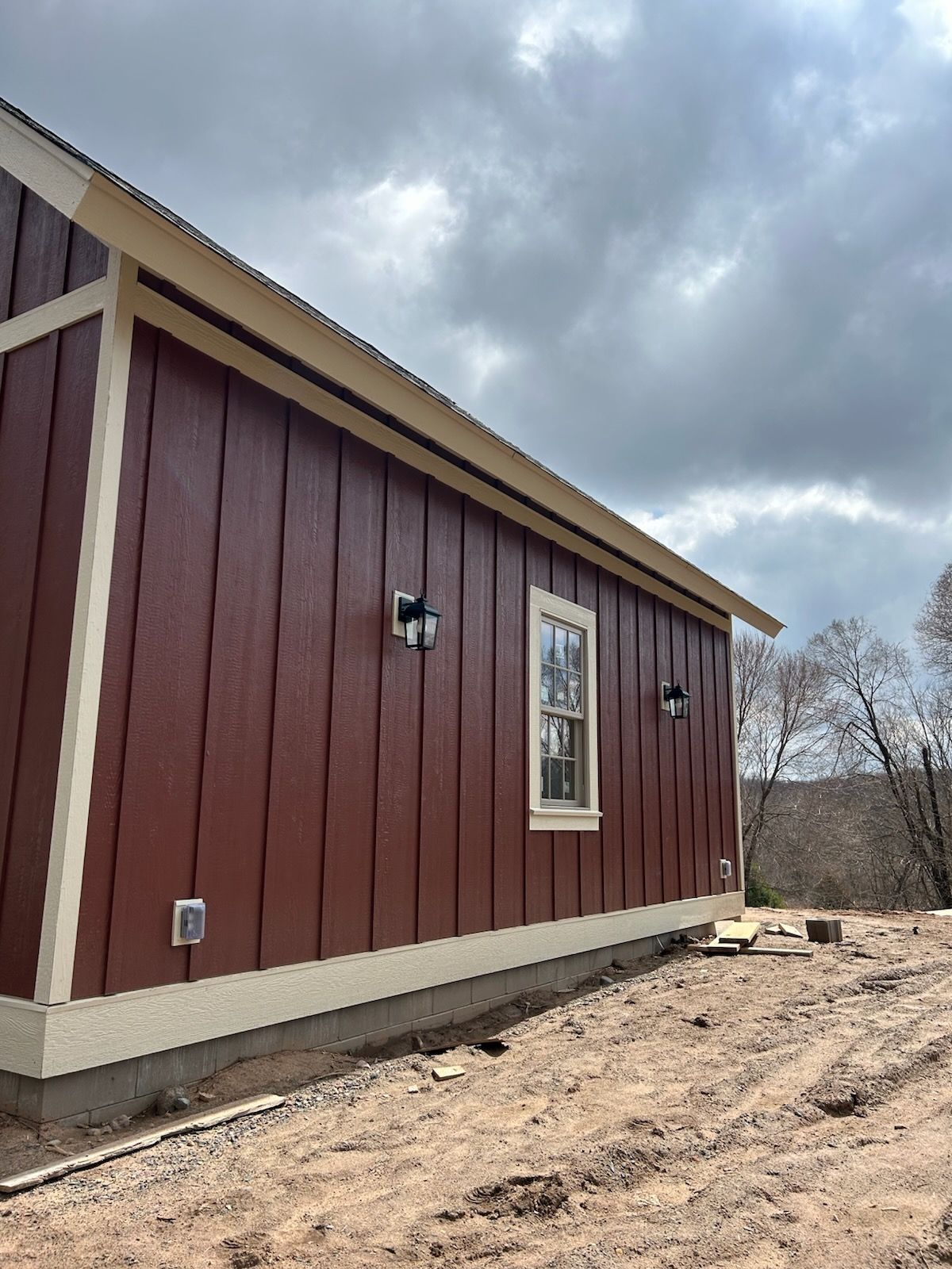 A red house with a white trim is sitting in the middle of a dirt field.