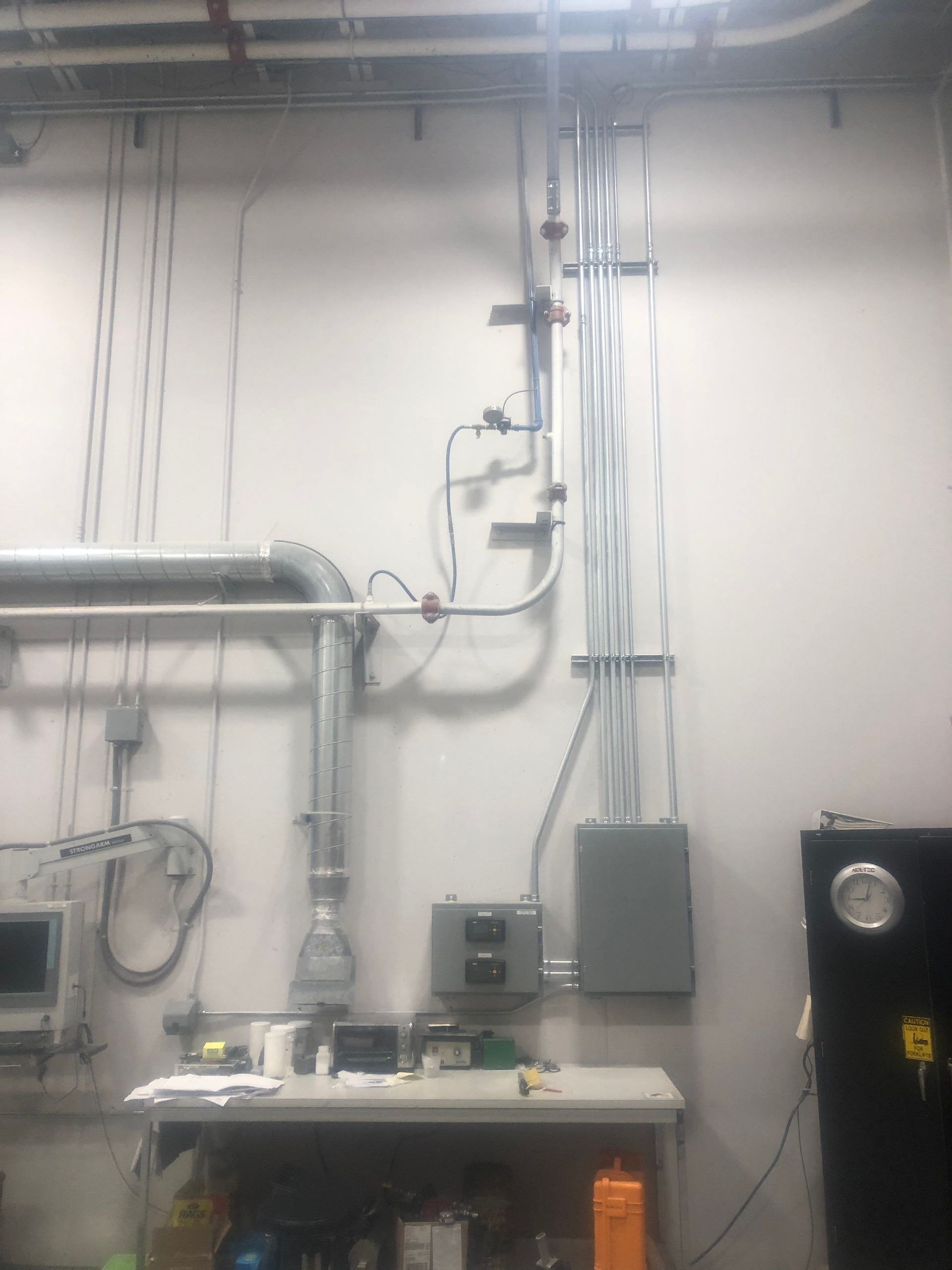 A room with a lot of wires hanging from the ceiling and a clock on the wall.