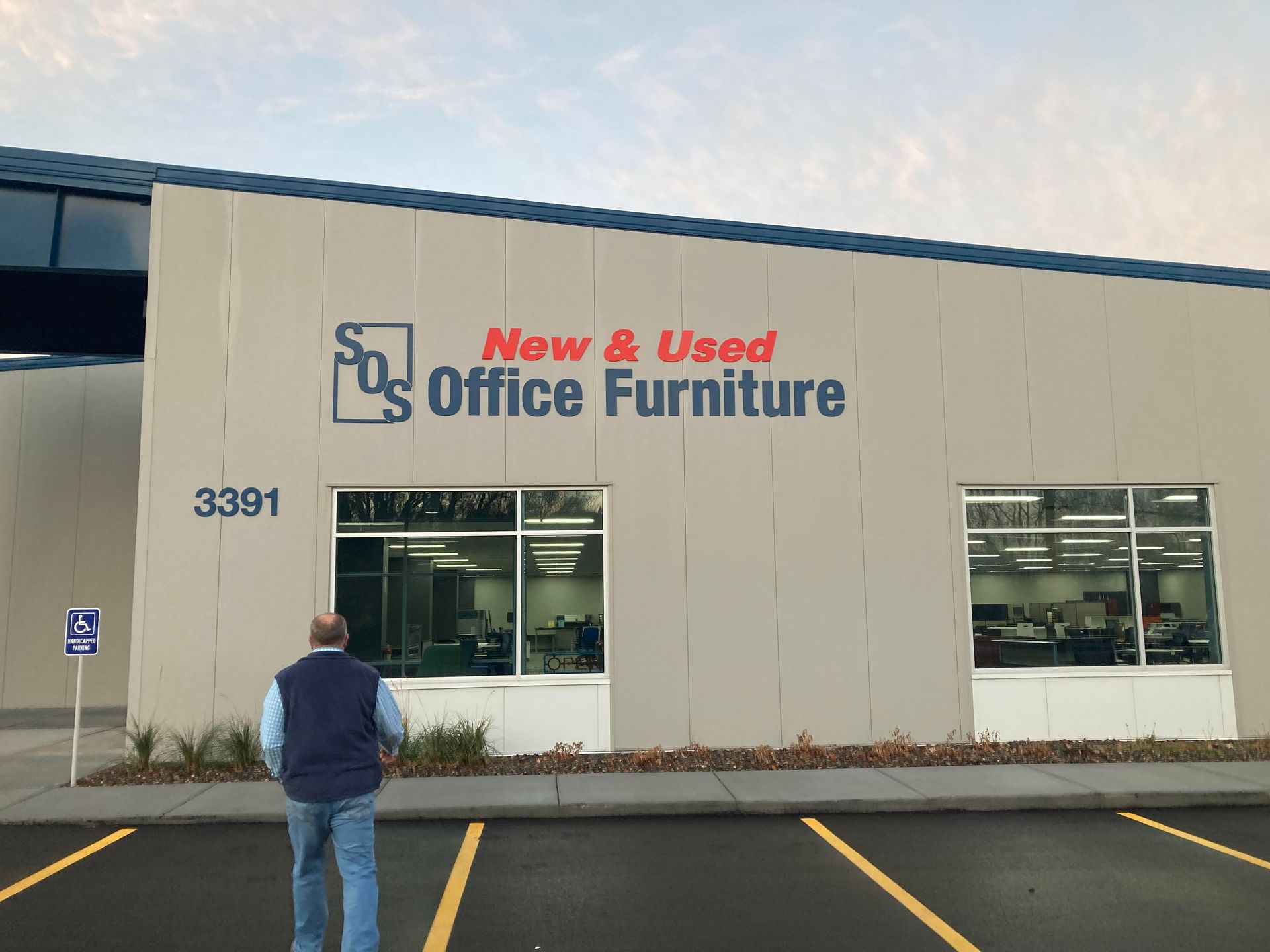 A man standing in front of a building that says new and used office furniture