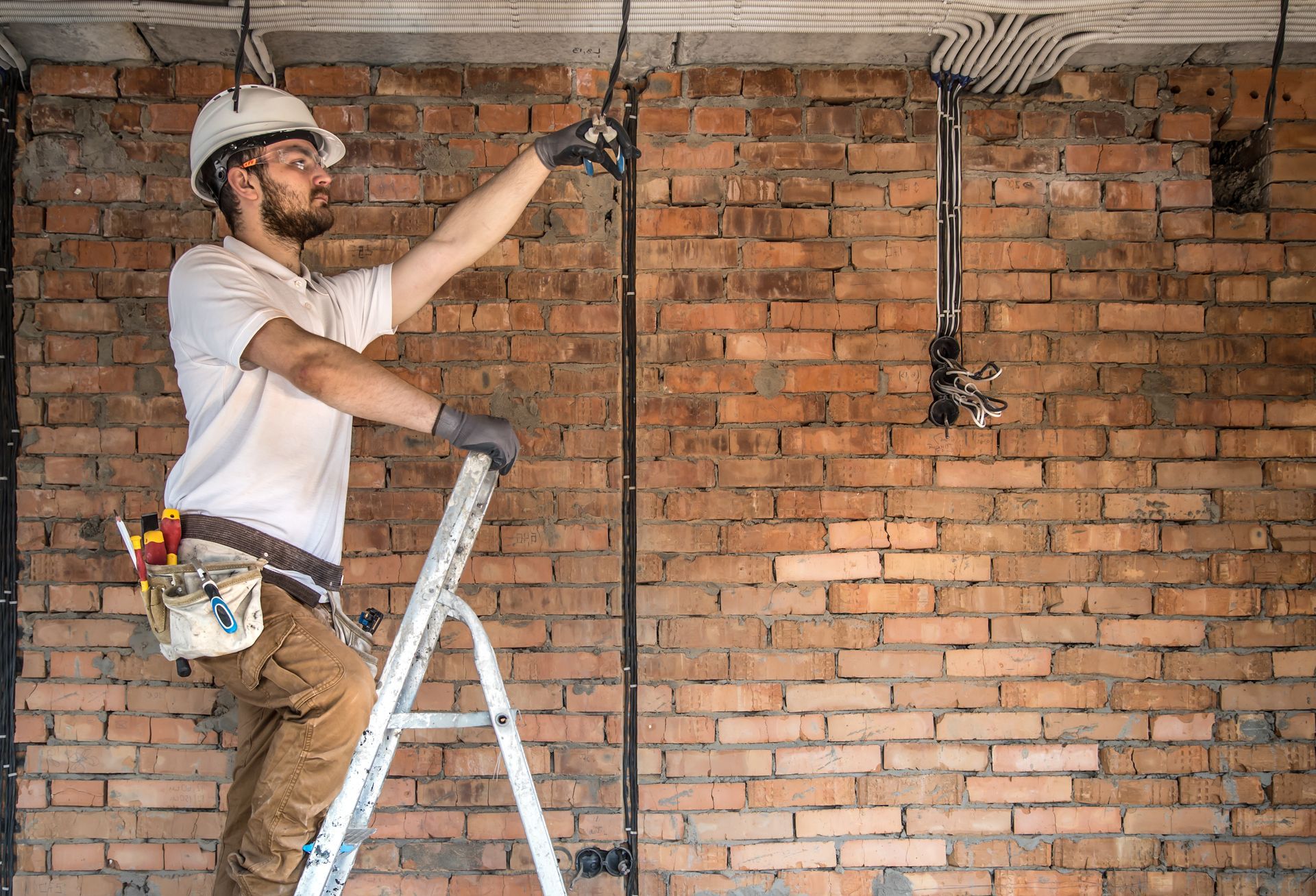 A man is standing on a ladder working on a brick wall.