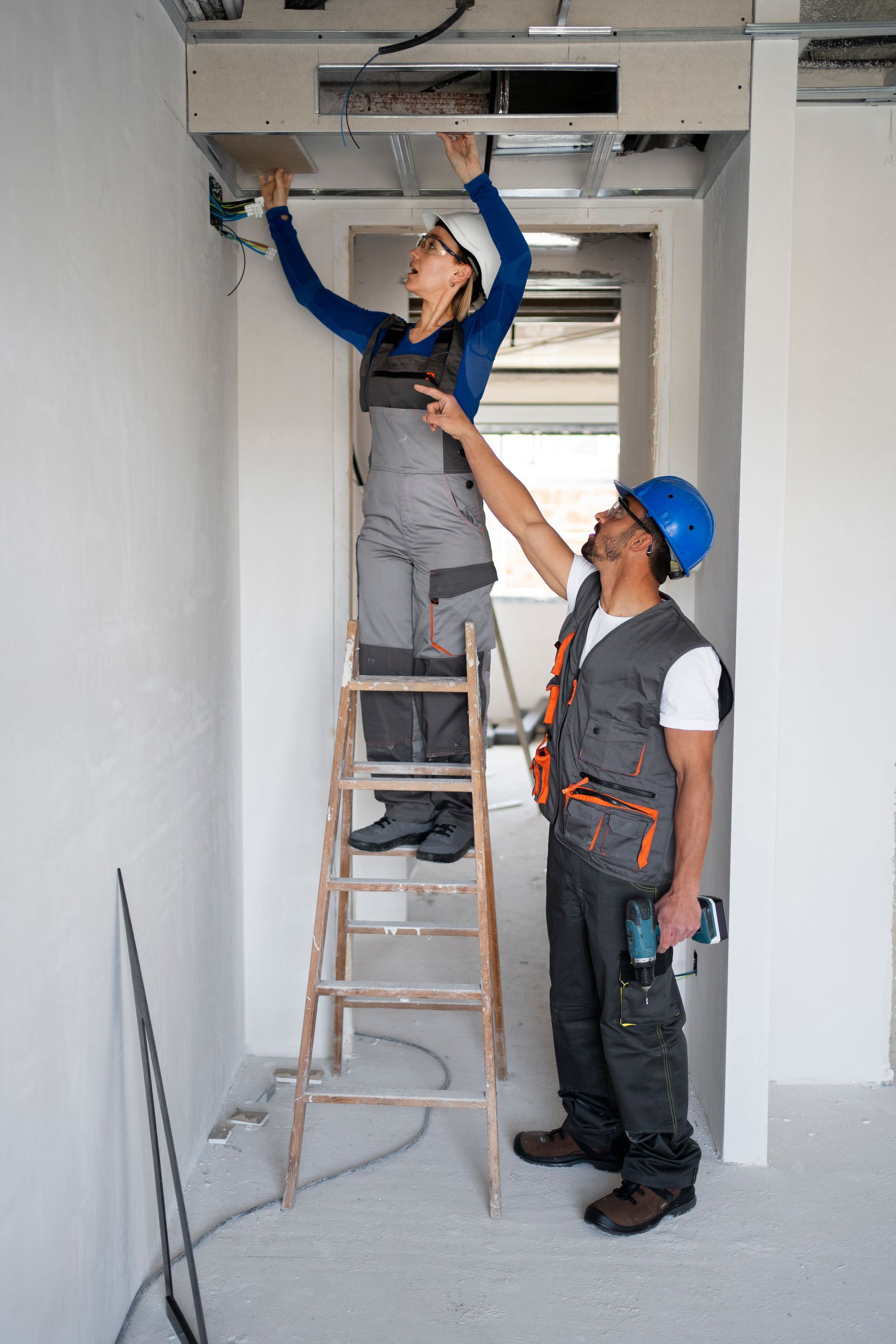 A man and a woman are working on a ceiling in a room.